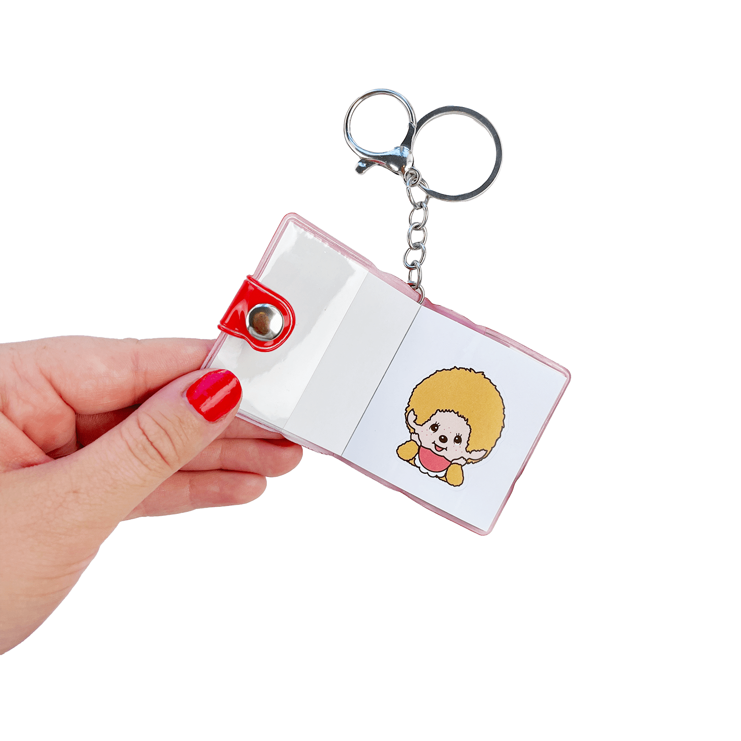 Hand holding open Monchhichi mini sticker book keychain showing kawaii Monchhichi character sticker inside — compact kawaii bag charm by Pipsticks