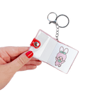 Hand holding open Monchhichi sticker book keychain featuring kawaii pink bunny character sticker — one of many cute designs inside this stationery girl bag charm