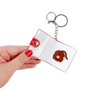 Hand holding open Monchhichi sticker book keychain to a different page — multiple kawaii character sticker designs inside this collectible mini bag charm by Pipsticks