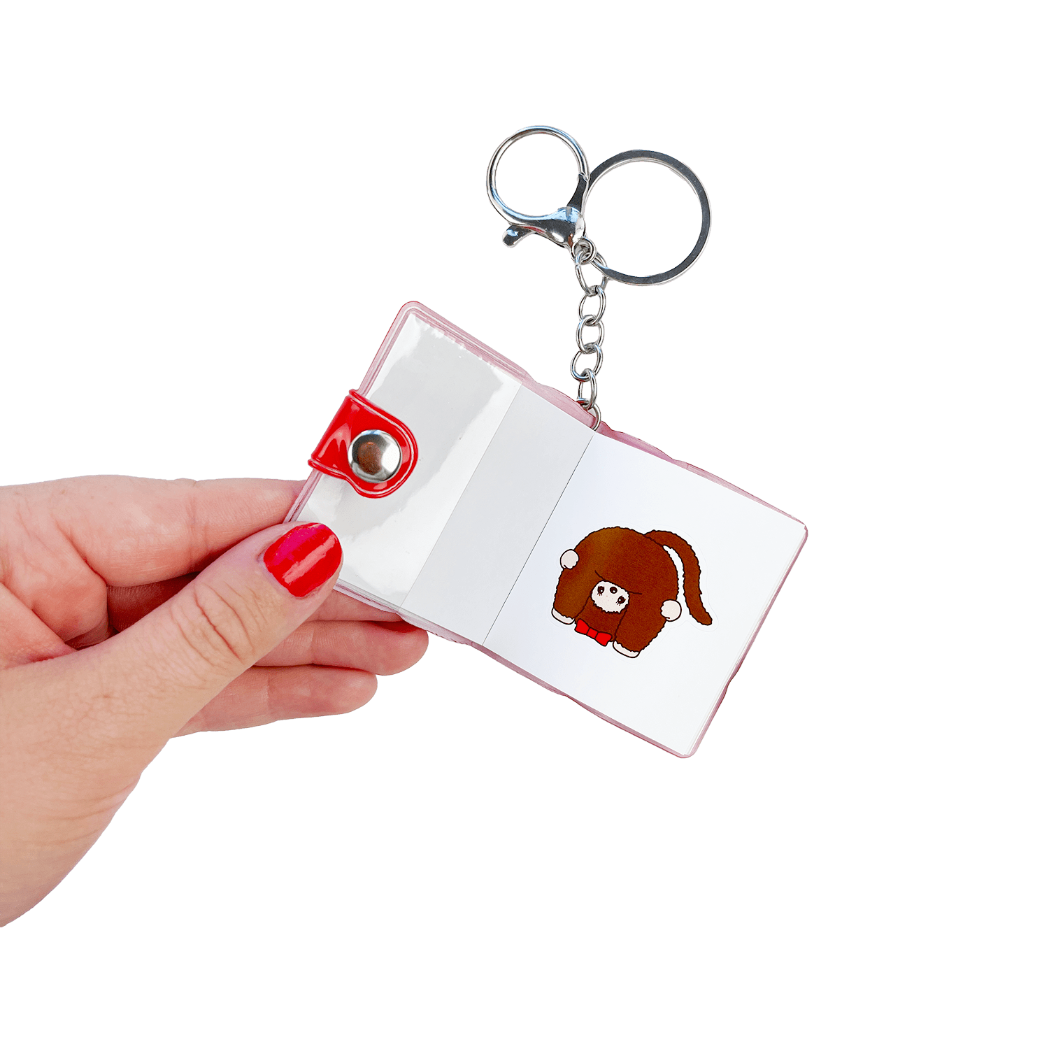 Hand holding open Monchhichi sticker book keychain to a different page — multiple kawaii character sticker designs inside this collectible mini bag charm by Pipsticks